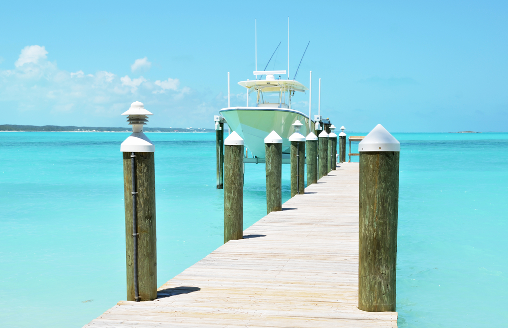 A boat docked on a pier in a tropical sea of Exuma Bahamas with clear waters, an image for the guide on how to get there.