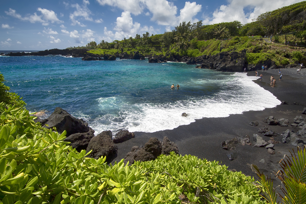 Waianapanapa State Park black sand beach on the Big Island with greenery in the foreground shows the concept of visiting Hawaii with or without a passport