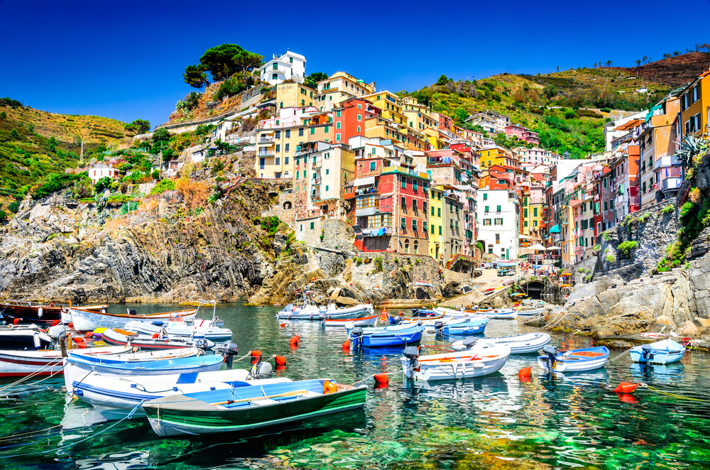 Riomaggiore in Cinque Terre, Italy shown from the water view with boats and colorful buildings under clear skies for a list of the best places to go in Italy