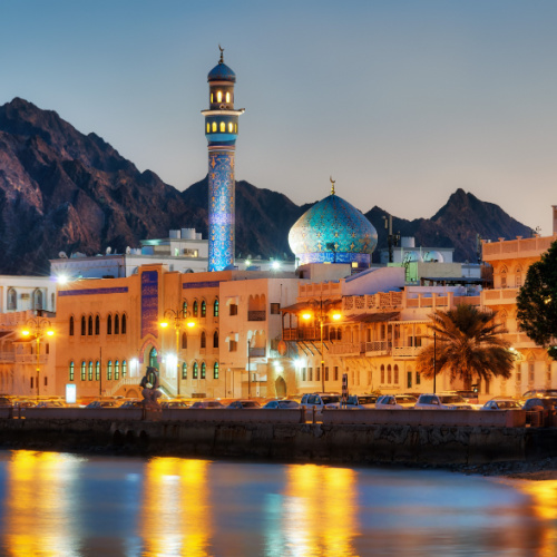 view from the sea during the best time to visit Oman, where the roof and the tower of the mosque can be seen peeking above the other town buildings during dusk.