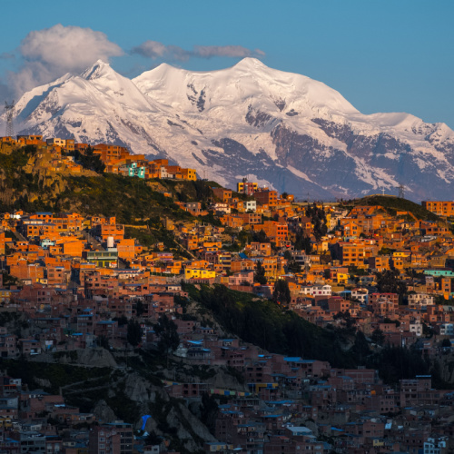 aerial photo of a populated city established on a hill near an icy mountain, during a sunset on one of the best time to visit Bolivia.