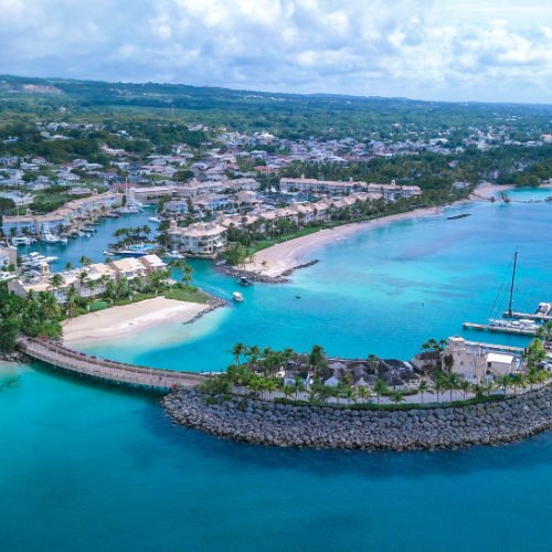 a coastal area with white sand and emerald waters, the land portion is filled with hotel structures, seen during the best time to travel Barbados.