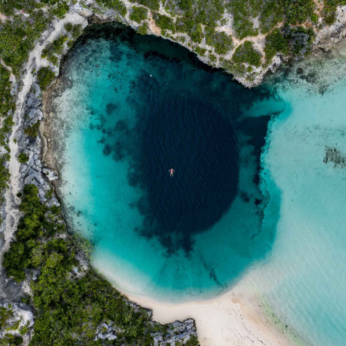 aerial view of an area of the beach with deeper portion and a dark center, where a person can be seen floating on the water during the best time to visit Bahamas.