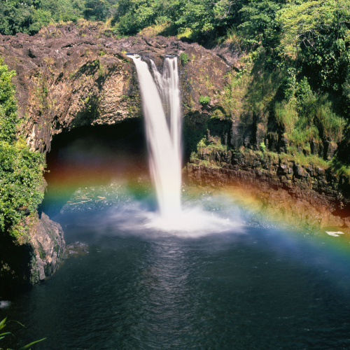 a waterfalls where behind the waterfalls seems like a cave, and a rainbow can be seen in front of the falls during the best time to visit the Big Island.