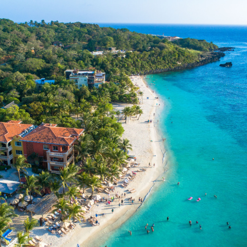 a beach where hotel structures are near the shore, and people can be seen enjoying the emerald waters, seen during one of the best time to visit Honduras.