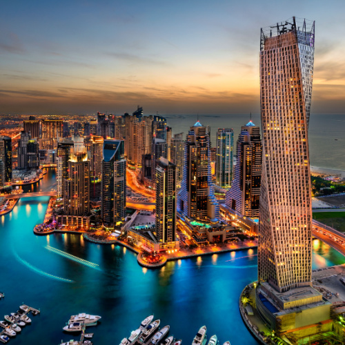 aerial view of a city with tall buildings with a river in the middle with boats docked on its pier, during dusk of the best time to visit Dubai.