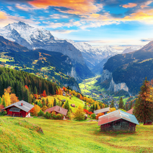 a country town where the houses are on the side of the mountain covered with green grass, with a view of tall mountain during sunset of the best time to visit Switzerland.