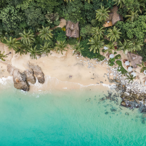 a top view of a beach with native houses concealed on the tree line and a calm emerald waters during the best time to visit Puerto Vallarta.