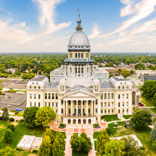 aerial view of a capitol building facing a park with pristine trees and grass and the rest of the town in background is filled wit trees during the best time to visit Illinois.