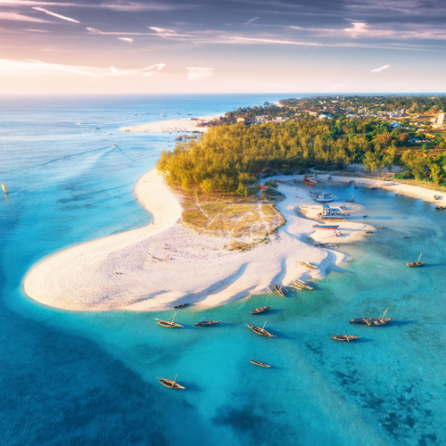 aerial view of an island with white sand and emerald waters, and several fishing boats can be seen on its shores during sunset of the best time to visit Zanzibar.