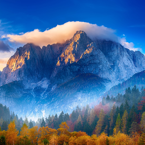 cloudy peak of a tall mountain and at the bottom is a misty forest furing the autumn season of the best time to visit Slovenia.