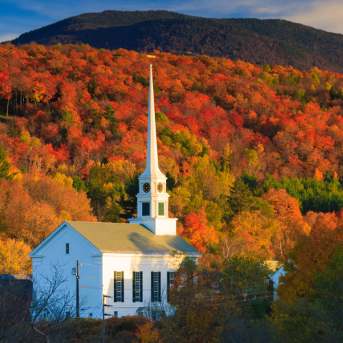 a church in a country during the best time visit New England in an autumn season where the building is surrounded by trees.