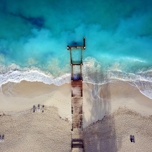 top view of a beach with a wooden dock that extends from the shore to the emerald waters, seen during a later afternoon of the best time to visit Turks and Caicos.