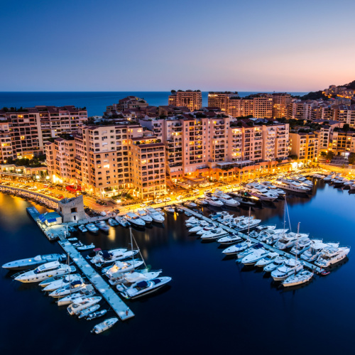 dusk of the best time to visit Monaco, where a coastal area filled with hotel structures can be seen where its pier is filled with docked boats.