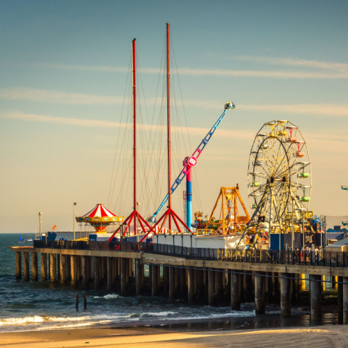 an amusement park in the beach built on an elevated platform above the waters where carnival rides can be seen during a sunset on one of the best time to visit New Jersey.
