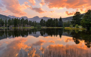 Gorgeous view of picturesque Sprague Lake, seen at dusk, with an orange sky overhead pictured during the best time to visit Rocky Mountain National Park