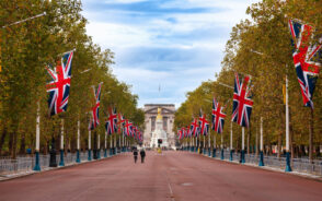 Pictured during the best time to visit London, a couple of people walking along the street under Union Jack flags outside of Buckingham Palace
