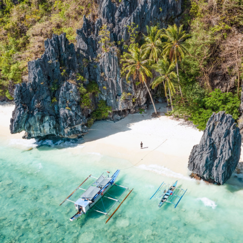 aerial view on a secluded area on an island with large rocks, and two boats can be seen docked on the white shore during the best time to visit the Philippines.