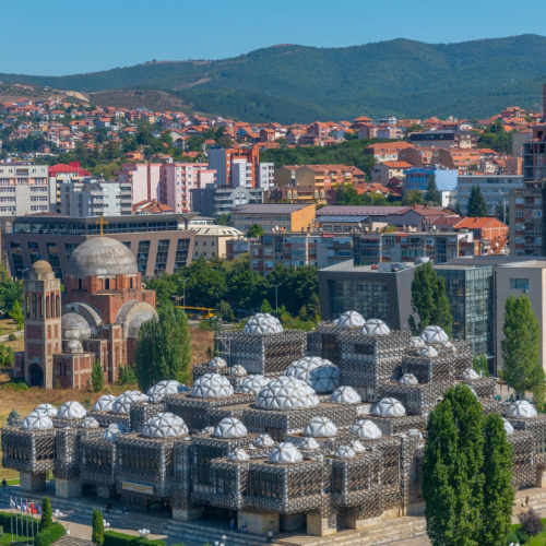 aerial view of a city with a unique struture where its roofs look like a golf ball, and in backgroud are commercial and residential area, seen during the best time to visit Kosovo.