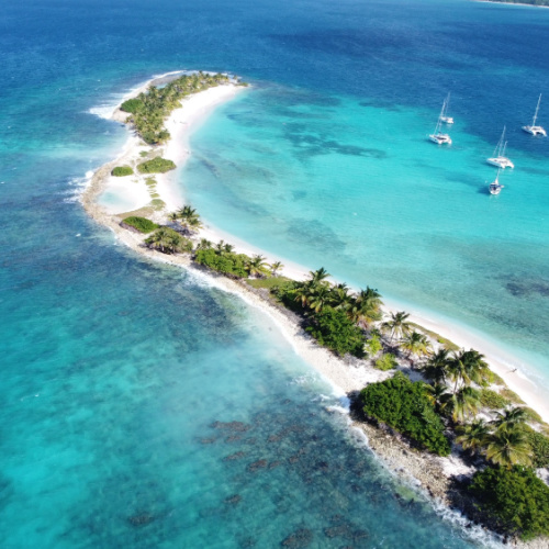 an elongated island with white sand and clear waters, where several boats can be seen docked near the beach on the best time to visit Grenada.