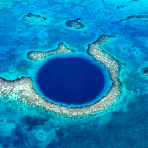 a blue round hole at the center of the sea, surrounded by a few small islands, seen on a top view during the best time to visit Belize.