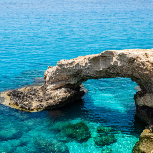 an arching rock formation in the coastal area the creates a bridge like formation, and at the bottom is a crystal clear water, during the best time to visit Cyprus.