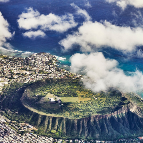 aerial view of a city near the sea with a large rounded area elevated from the plain ground, during a cloudy afternoon on the best time to visit Oahu.