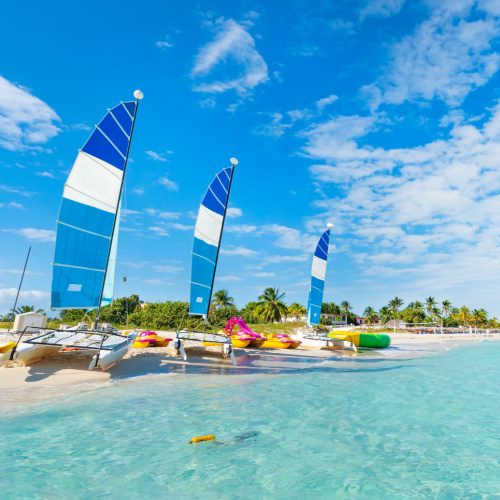 several sailing boats placed of the white shore of a beach with clear waters during an afternoon of the best time to visit Cuba.