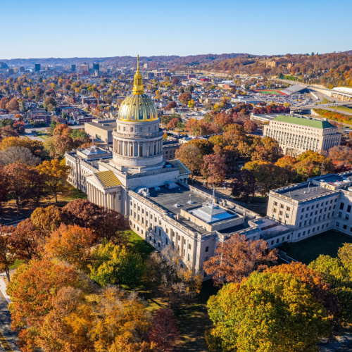 a capitol building surrounded by trees and the rest of the town is visible at a distance, photographed during one of the best time to visit West Virginia.