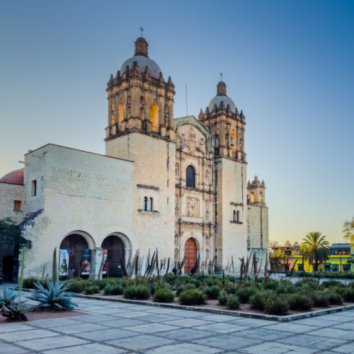 an old church facing an empty square planted with several plants, seen during the best time to visit Oaxaca.