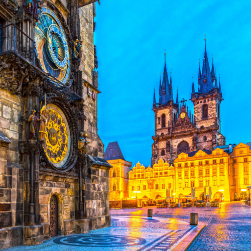 beautiful old marking on a building with a huge clock, and visible in background is an illuminated old church building during a dusk on the best time to visit Prague.