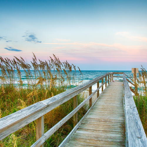 a boardwalk that extends to the shore of a beach where summer grass can be seen with calm waters during the one of the best time to visit North Carolina.