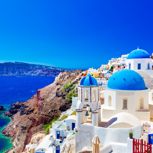 a view at a coastal town on the side of a mountain where all the structures are white and the sea at the bottom is blue during the best time to visit Greece.