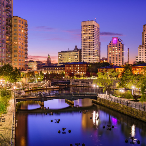 a view during dusk on one of the best time to visit Rhode Island, where the city skyline can be seen and a bridge where people are crossing.