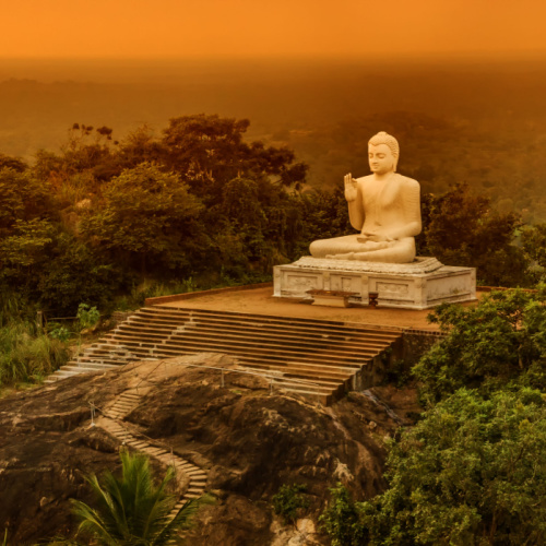 a white statue of buddha in a peak of a mountain with stairs, during a sunset of the best time to visit Sri Lanka.