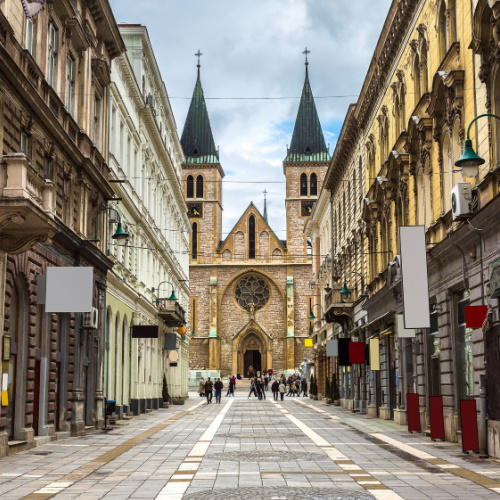 a view in an street during the best time to visit Bosnia where old buildings are on each side of the street and on the end is a historical church building.