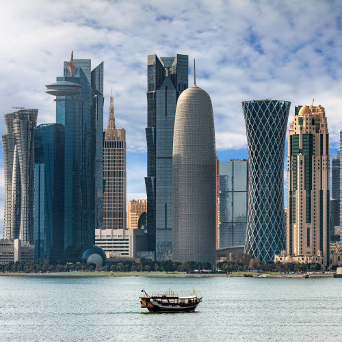 a small ferry passing near a city with tall unique modern skyscrapers during the best time to visit Qatar.