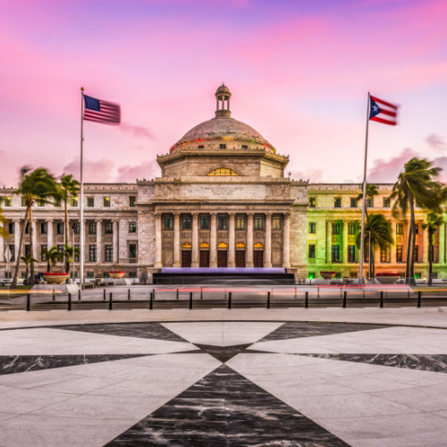 a capitol building with two flags hanging on its pole during a sunset of the best time to visit Puerto Rico.