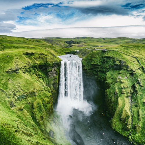 a tall waterfalls surrounded by green mountains on a cloudy day of the best time to visit Iceland.