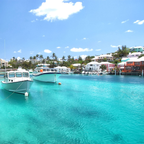 a coastal area filled with hotel structures where two boats can be seen anchored near the beach, in an afternoon during the best time to visit Bermuda.