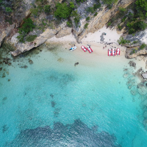 top view of a beach with white sand and emerald clear calm waters, with a few boats on the shore, during the best time to visit Anguilla.