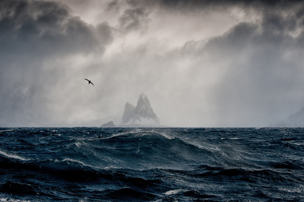 Elephant Island in the heart of winter during the worst time to visit Antarctica with giant waves in front of the viewer and a gloomy sky blanketing the island in the distance