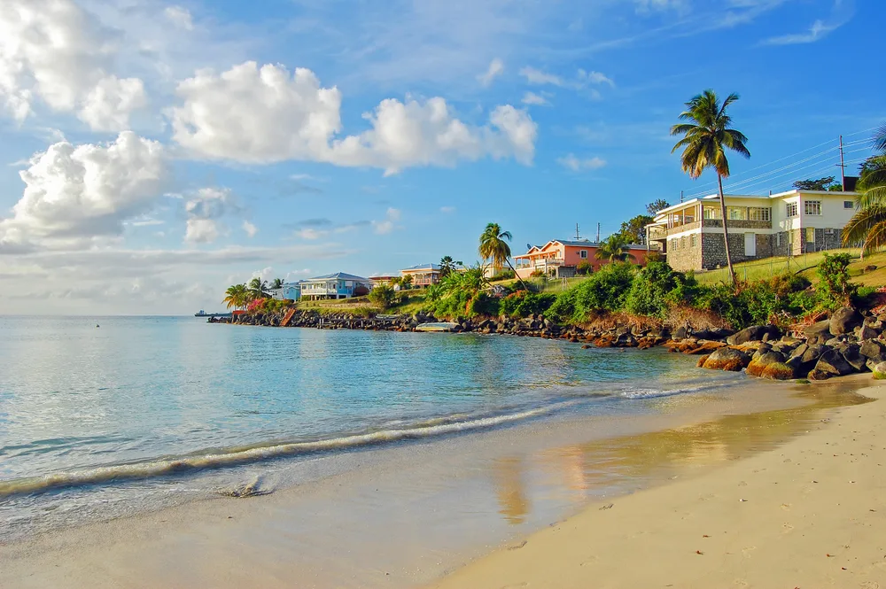 Picturesque view of Grand Anse Beach pictured with clouds overhead with rocks and vegetation jutting out into the ocean during the best time to visit Grenada