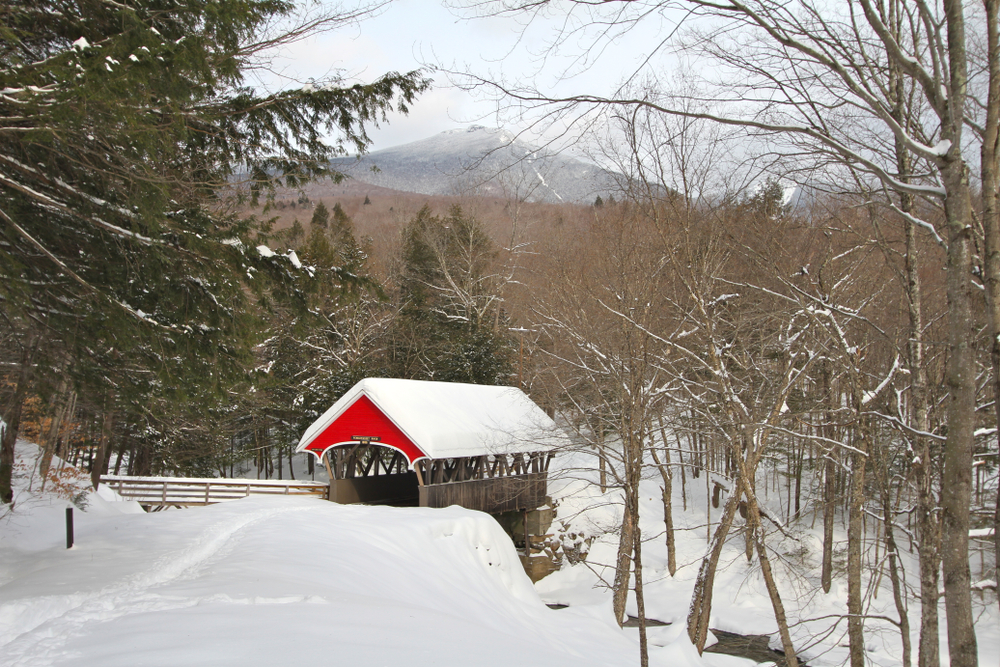 Red wooden snow covered bridge pictured in New Hampshire during the winter, the overall worst time to visit