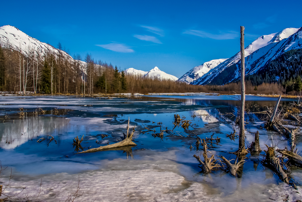 Partially frozen lake near Anchorage during the cheapest time to visit with snow on the mountains in the background of the image