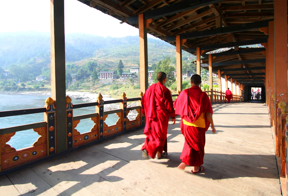 Picturesque view of two red-robed monks walking along the sidewalk in the Puna Mocchu Bazam bridge during the summer, the overall least busy time to visit Bhutan