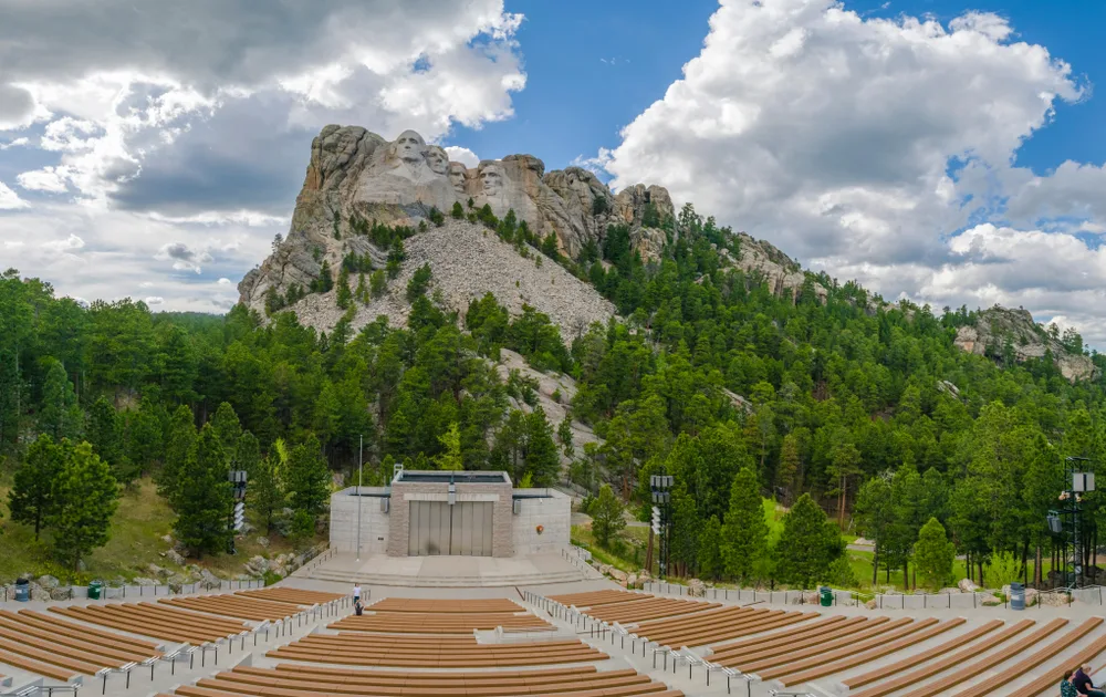 Unique view of Mount Rushmore pictured from the top steps of the amphitheater, as seen on a blue-sky day with a few clouds in the sky
