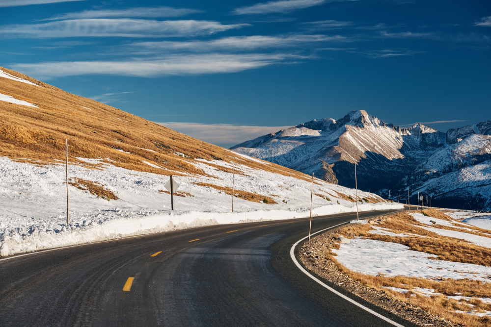 View of frozen Trail Ridge Road pictured in the winter with snow-capped mountains and snowy roads pictured under a blue sky during the best time to visit Rocky Mountain National Park