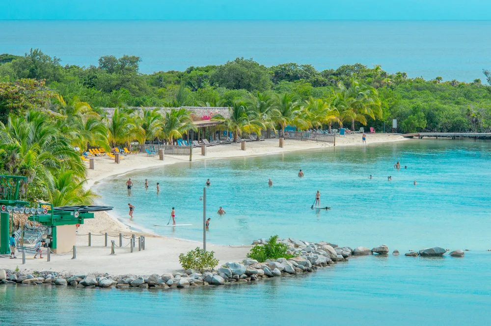 Few people on a beach on Roatan Island in Honduras, pictured during the best time to visit, with lush greenery surrounding the white sand island