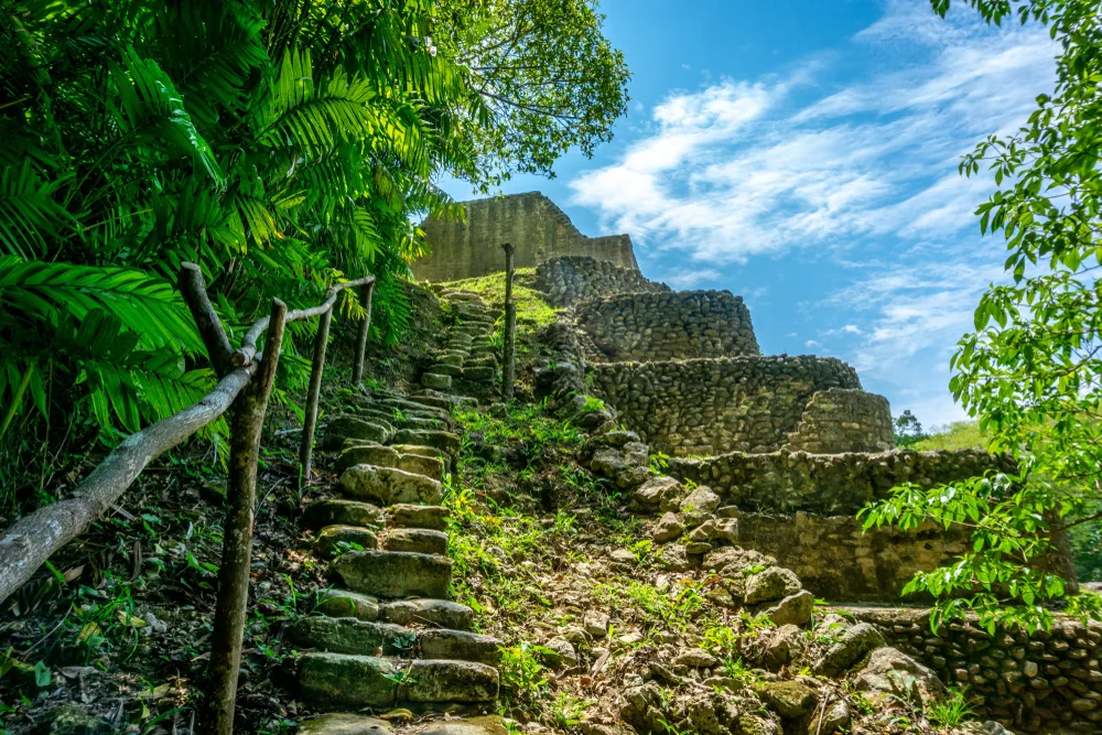 Very old stone steps going up Caracol Temple and Archeological Reserve in San Ignacio, Belize, during the best time to visit with blue skies peppered with clouds overhead